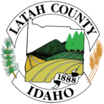 Latah County logo - white ribbons with black text curved in a cirlce, with wheat and pine needles. A shape of latah county with wheat fields, farm fields and trees and hills in the distance.